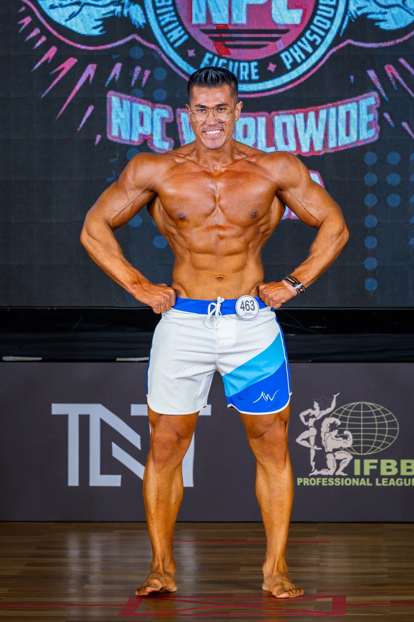 Hussain on stage at an NPC Worldwide physique show, front pose
